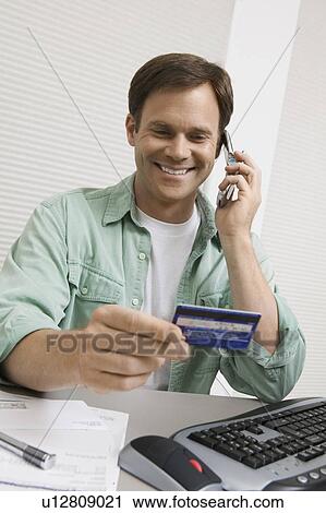 Stock Image - Man Using Credit Card to Order Over Phone. Fotosearch