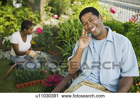 Man using laptop in garden, wife watering plants in background, (portrait) View Large Photo Image Stock Image - Man using laptop in garden, wife watering plants in background, (portrait). Fotosearch