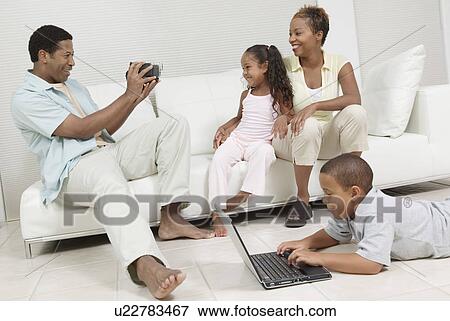 Man Videotaping Family sitting on sofa View Large Photo Image Stock Photo - Man Videotaping Family sitting on sofa. Fotosearch