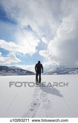 Stock Image - Man walking in snowshoes through snow, back view. Fotosearch