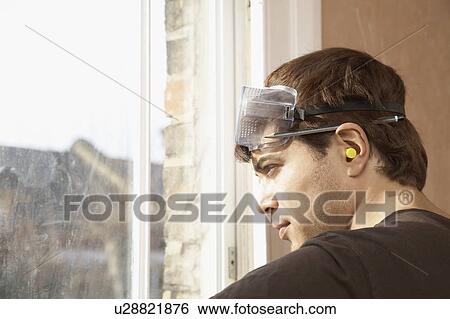 Stock Photograph - Man wearing goggles and earplugs, looking out window. Fotosearch