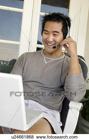 Stock Photo - Man wearing headset using laptop on porch. Fotosearch