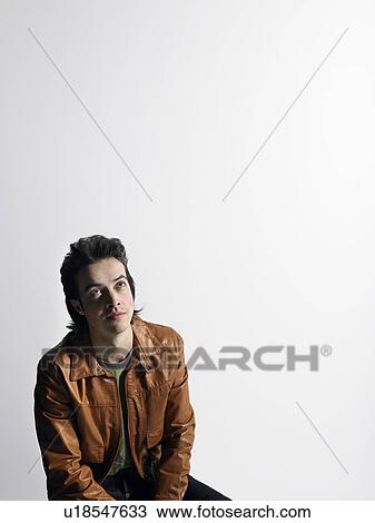 Stock Image - Man wearing leather coat, sitting in studio. Fotosearch