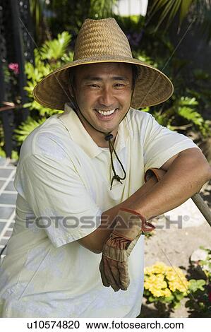 Stock Image - Man wearing straw hat in garden, (portrait). Fotosearch