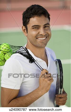 Stock Photo - Man with on tennis court with tennis balls and racket, portrait. Fotosearch