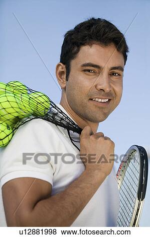 Stock Photo - Man with tennis balls and racket outdoors, portrait. Fotosearch
