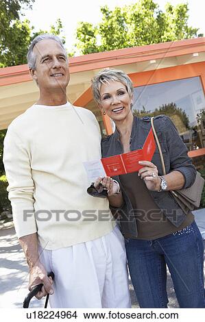 Mature couple holding suitcase and brochure outside View Large Photo Image Picture - Mature couple holding suitcase and brochure outside. Fotosearch