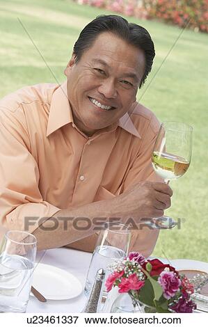 Mature man sitting at outdoor table, holding wine glass, View Large Photo Image Stock Photo - Mature man sitting at outdoor table, holding wine glass,. Fotosearch