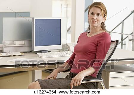 Mid-adult female office worker sitting in cubicle, portrait View Large Photo Image Picture - Mid-adult female office worker sitting in cubicle, portrait. Fotosearch