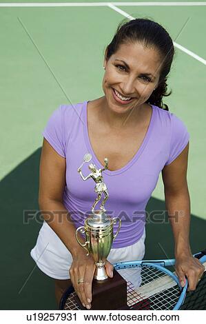 Stock Image - Mid-adult female tennis player on court holding trophy, portrait, high angle view. Fotosearch