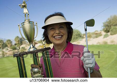 Picture - Middle-age woman holding golf trophy, smiling, (portrait). Fotosearch