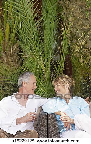 Stock Photography - Middle-aged couple sitting outdoors on chairs talking. Fotosearch