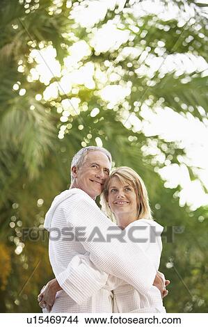 Middle-aged couple standing by palm trees hugging, portrait View Large Photo Image Picture - Middle-aged couple standing by palm trees hugging, portrait. Fotosearch