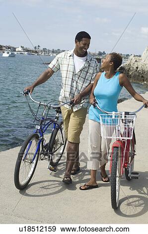 Stock Photo - Middle-aged couples standing at promenade with bicycles. Fotosearch