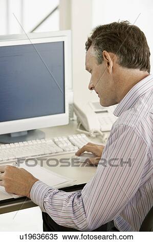 Stock Photography - Middle-aged male office worker sitting in cubicle writing. Fotosearch