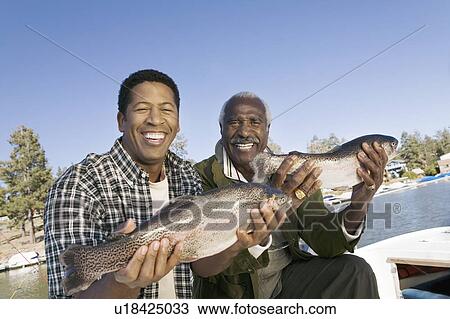 Stock Image - Middle-aged man and son showing fishes, smiling, (portrait). Fotosearch
