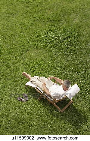 Middle-aged man reclining on lawn in deck chair, reading, high angle view View Large Photo Image Stock Image - Middle-aged man reclining on lawn in deck chair, reading, high angle view. Fotosearch