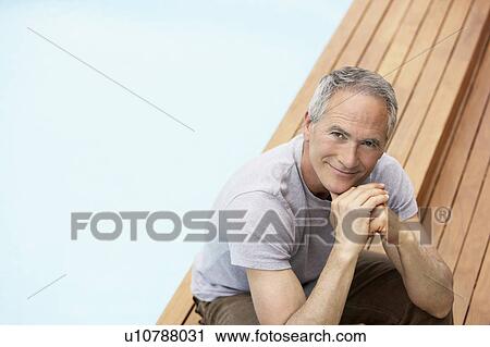 Stock Image - Middle-aged man sitting by pool, portrait, high angle. Fotosearch