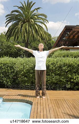 Stock Photo - Middle-aged man standing by swimming pool with arms outstretched doing tai chi. Fotosearch