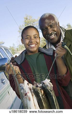 Stock Photo - Middle-aged man with grandson holding fishes, smiling, (portrait). Fotosearch