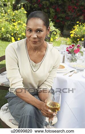 Middle aged woman sitting at table, holding wine glass, outdoors View Large Photo Image Stock Image - Middle aged woman sitting at table, holding wine glass, outdoors. Fotosearch