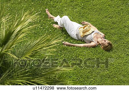 Stock Photo - Middle-aged woman sleeping on grass, high angle view. Fotosearch