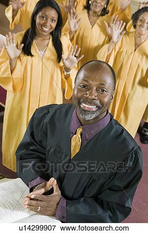 Stock Photo - Minister at altar with Bible, gospel choir in background, portrait. Fotosearch