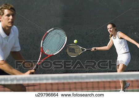 Picture - Mixed Doubles player hitting tennis ball, partner standing near net. Fotosearch