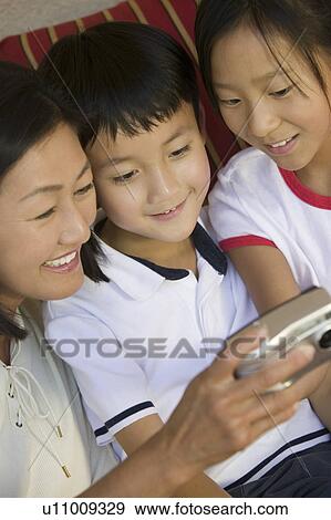 Stock Photo - Mother and Children on sofa Looking at pictures on Digital Camera, close up. Fotosearch
