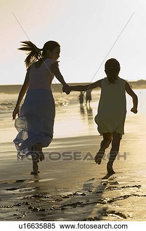 Stock Photography - Mother and daughter (7-9) running on beach. Fotosearch