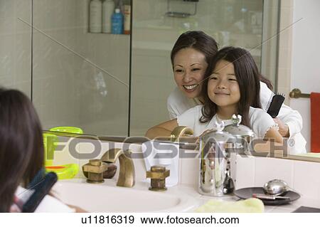 Stock Photo - Mother and Daughter Looking at reflection in Bathroom mirror, focus on mirror. Fotosearch