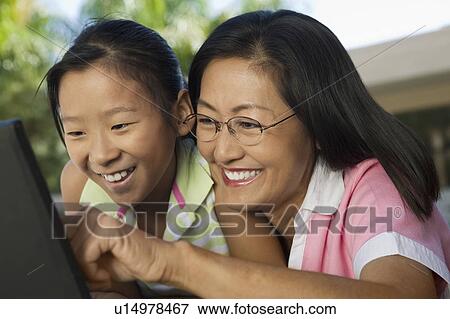 Stock Photo - Mother and Daughter sitting at backyard table Using Laptop Together, close up. Fotosearch