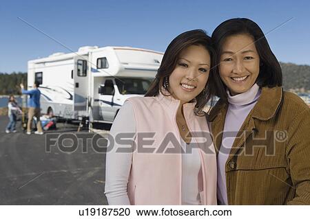 Stock Image - Mother and teenage daughter standing outside of RV at lake. Fotosearch