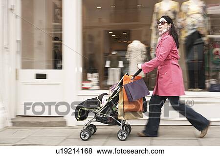 Mother pushing stroller by clothes shop on street View Large Photo Image Stock Photo - Mother pushing stroller by clothes shop on street. Fotosearch