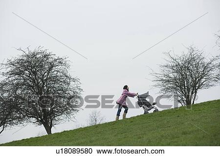Stock Image - Mother pushing stroller uphill. Fotosearch
