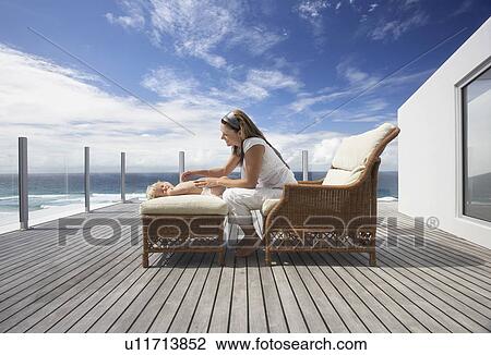 Mother sitting in wicker sofa, Playing with Son on ottoman on wooden porch, side view View Large Photo Image Stock Image - Mother sitting in wicker sofa, Playing with Son on ottoman on wooden porch, side view. Fotosearch