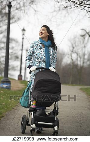 Stock Photo - Mother walking with baby carriage in park. Fotosearch
