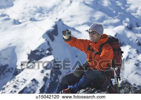 Stock Image - Mountain climber taking a picture on mountain peak. Fotosearch