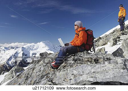 Stock Photo - Mountain climber using laptop on mountain peak. Fotosearch