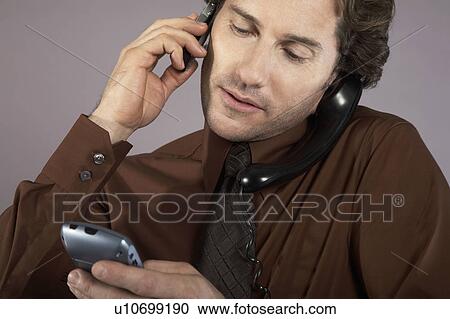 Stock Image - Multi-tasking businessman using mobile phone. Fotosearch