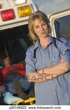 Stock Image - Paramedic stands with arms folded near ambulance. Fotosearch