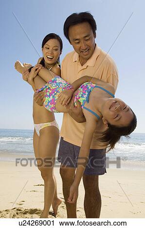 Stock Image - Parents carrying daughter (7-9) on beach. Fotosearch