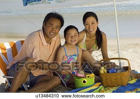 Stock Image - Parents with daughter (7-9) having picnic on beach, (portrait). Fotosearch