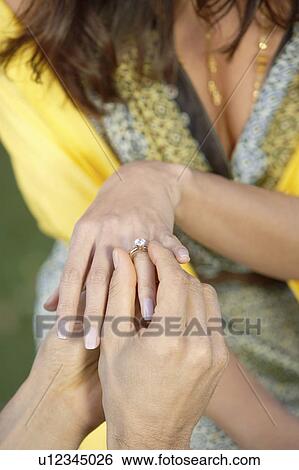Stock Photograph - Placing Wedding Ring on Woman's Finger, mid section, close-up. Fotosearch