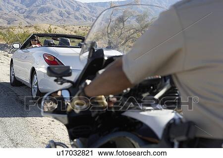 Stock Image - Police officer on motorbike stopping car on desert road side. Fotosearch