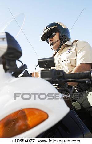 Stock Photo - Police officer sitting on motorcycle, low angle view, (low angle view). Fotosearch