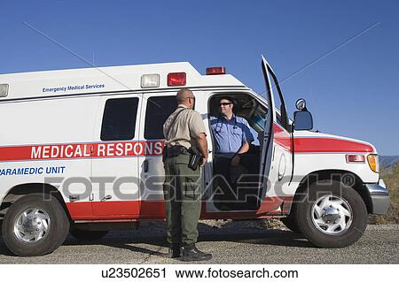 Stock Image - Policeman talks to paramedic at vehicle. Fotosearch