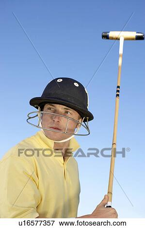 Stock Photo - Polo Player wearing helmet with face mask, holding polo stick, side view. Fotosearch