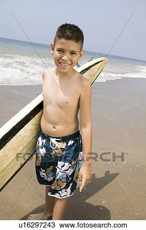 Stock Image - Portrait of boy holding surfboard on beach. Fotosearch