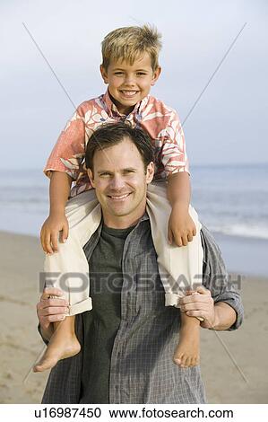 Stock Image - Portrait of boy on fathers shoulders at beach. Fotosearch